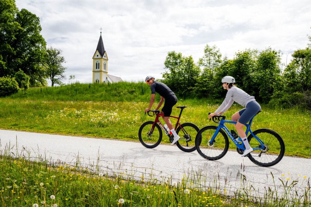 Pärchen fährt mit Rad. Im Hintergrund eine Kirche